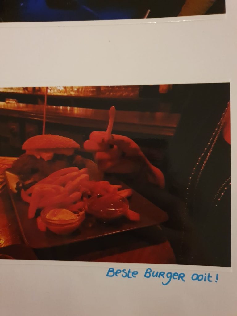 Foto van een foto uit een album van de 'de beste burger ooit!', kipburger met frites en sauzen.