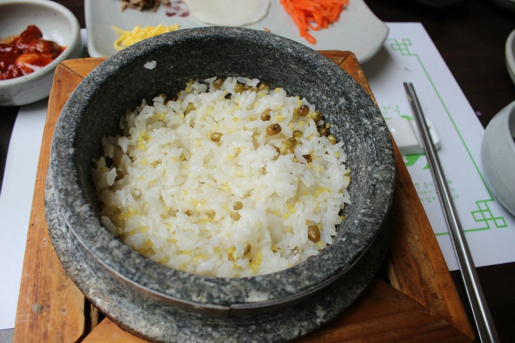 Een koreaanse Dolsot op een tafel met bijgerechten, rijst en metalen stokjes.